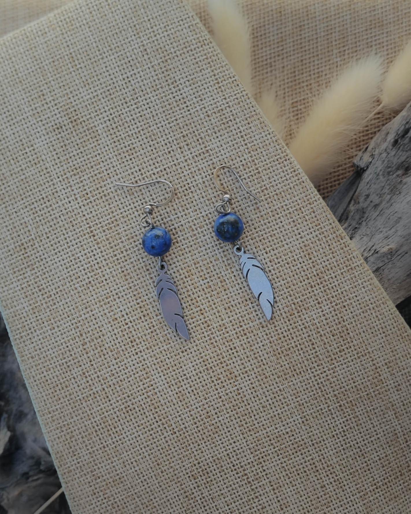 Vue de dessus des boucles d’oreilles Lapis Lazuli motif plume acier mettant en valeur la pierre et le détail du motif