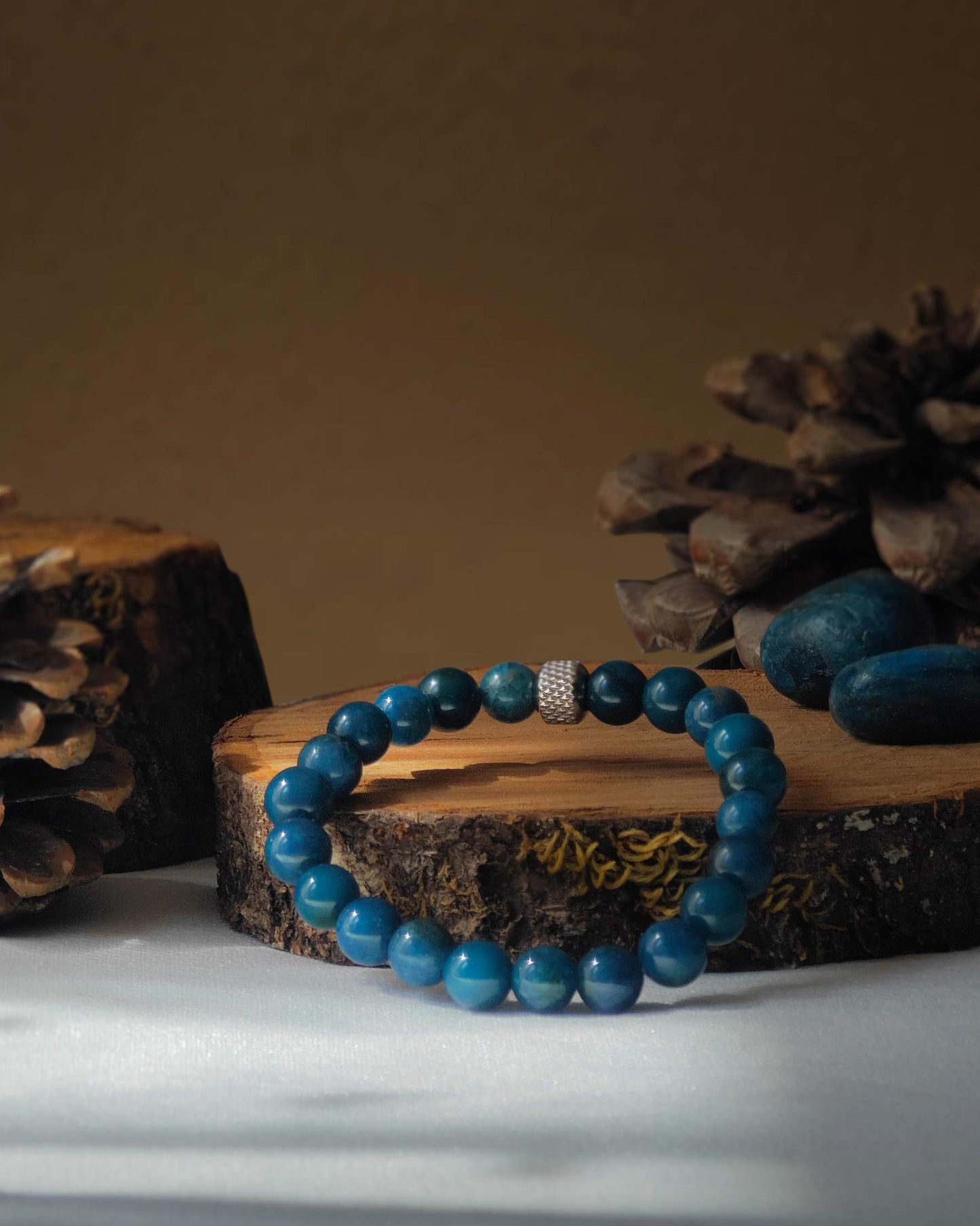 Bracelet en apatite naturel pose sur rondelle de bois avec pomme de pin et pierre polie d apatite
