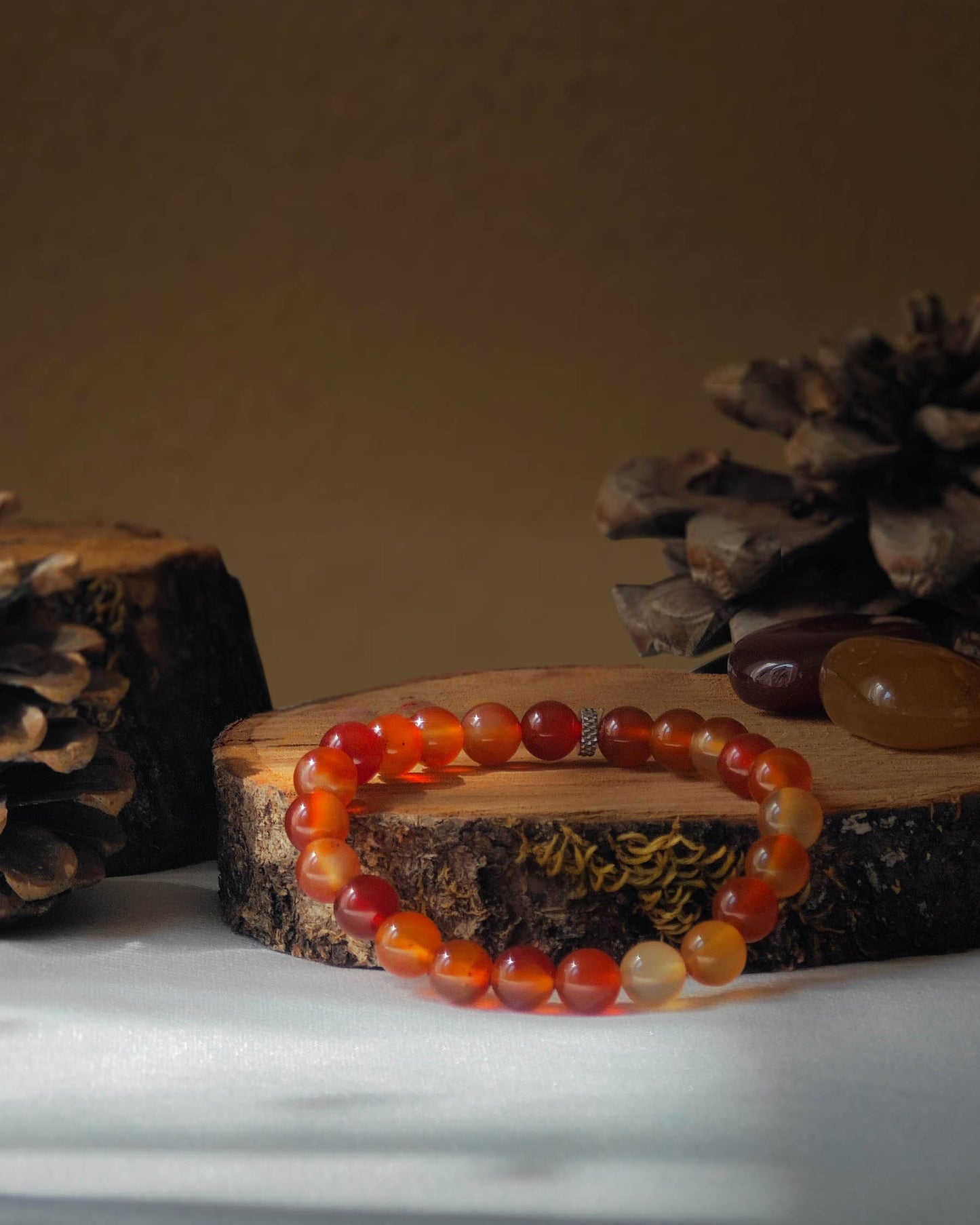 Bracelet en cornaline naturel pose sur rondelle de bois avec pomme de pin et pierre polie de cornaline