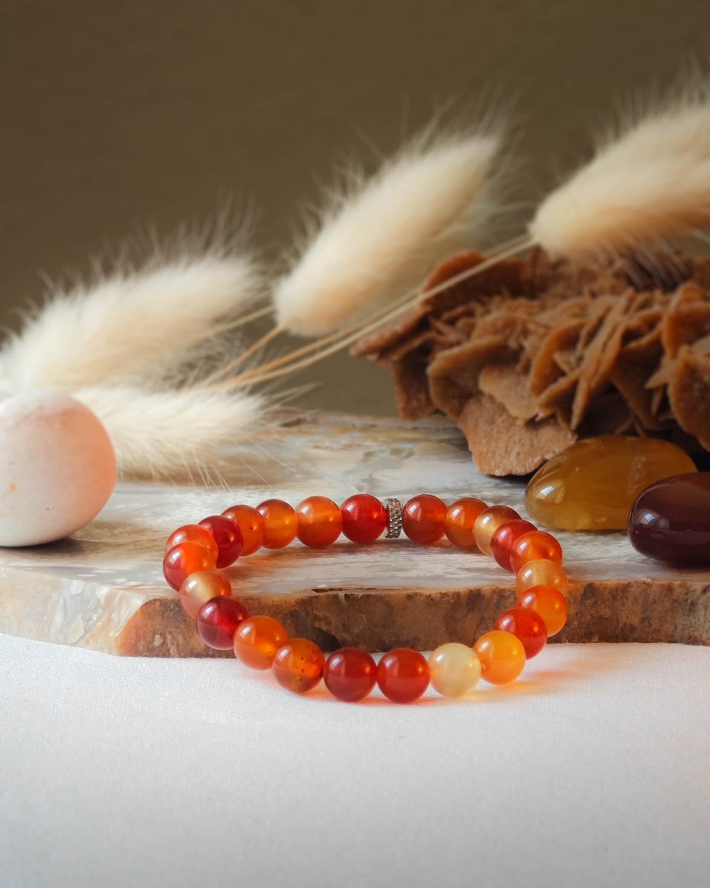 Bracelet en cornaline naturel pose sur roche lisse avec epis blancs et pierre polie de cornaline