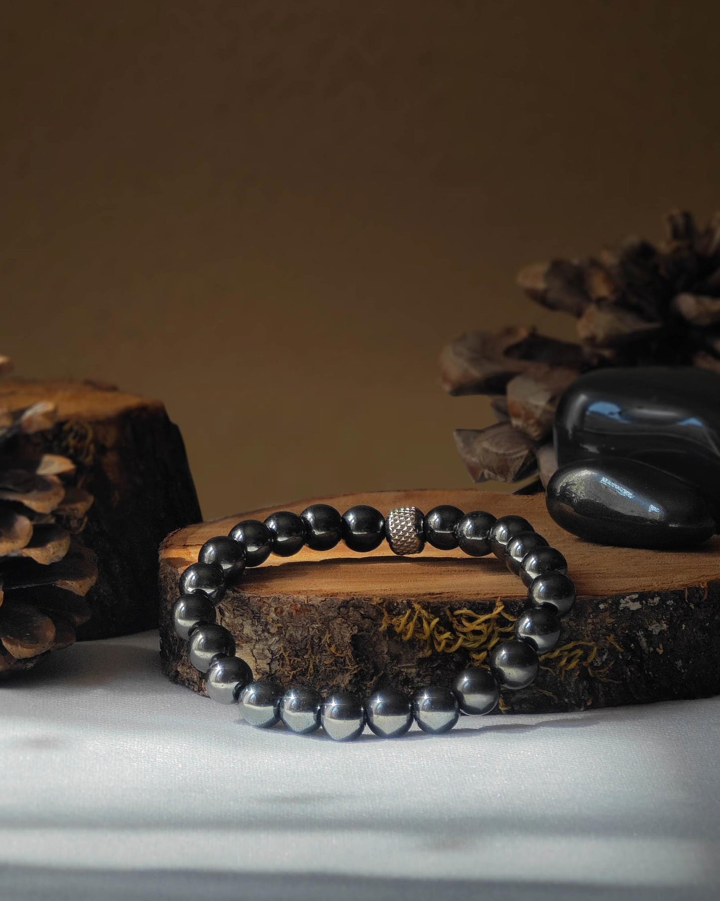 Bracelet en hematite naturel pose sur rondelle de bois avec pomme de pin et pierre polie d hematite