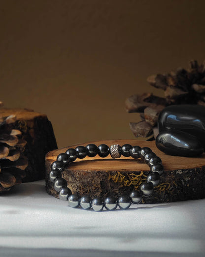 Bracelet en hematite naturel pose sur rondelle de bois avec pomme de pin et pierre polie d hematite