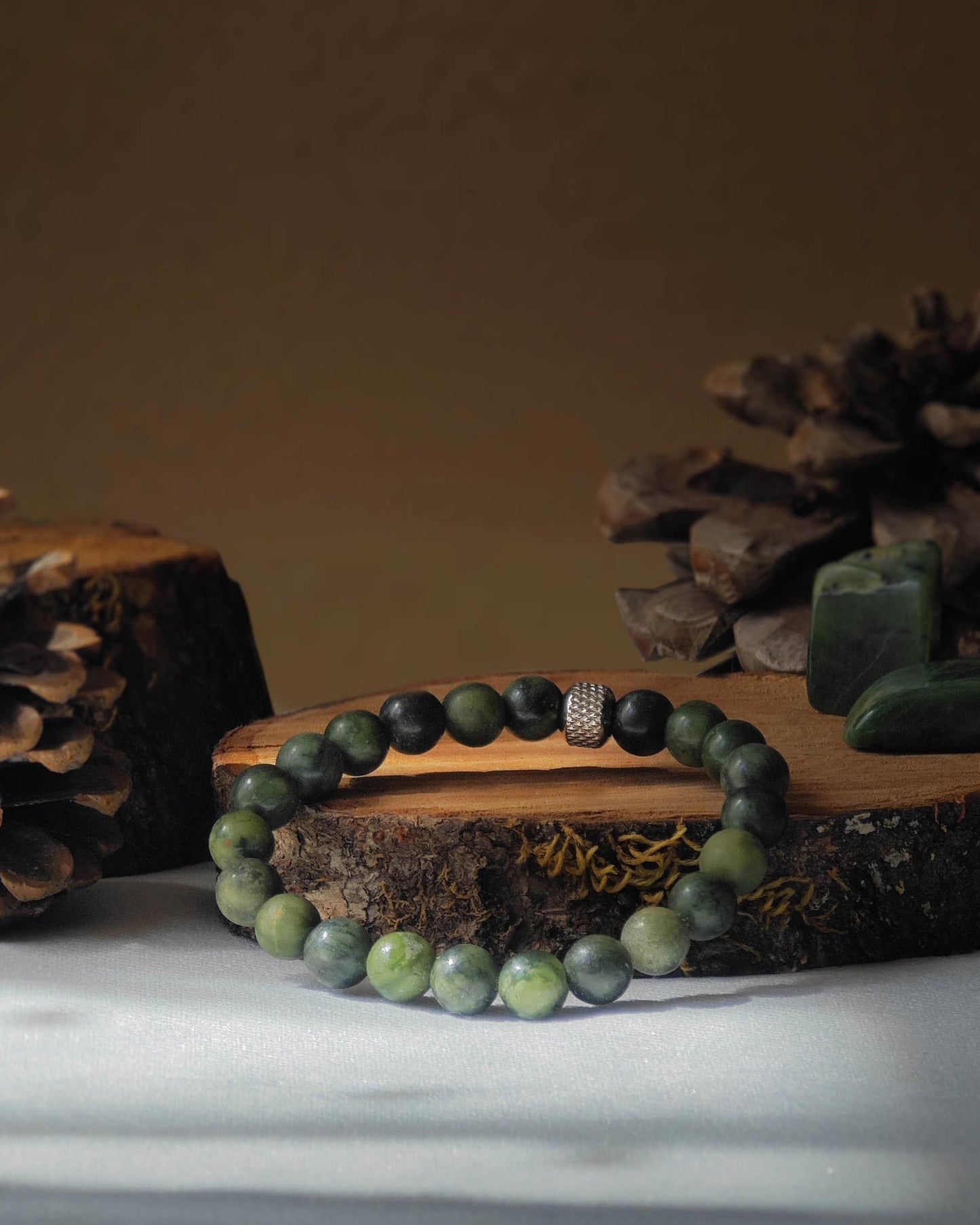 Bracelet en jade verte naturel pose sur rondelle de bois avec pomme de pin et pierre polie de jade verte