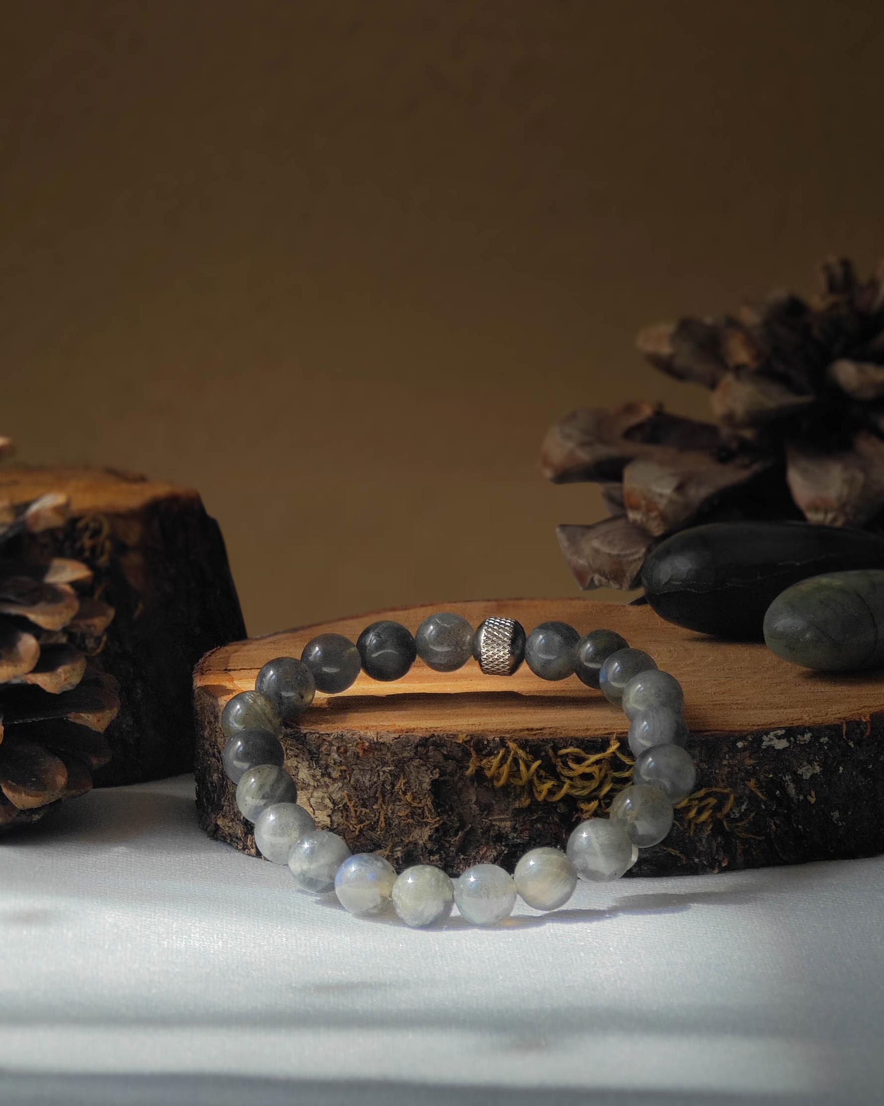 Bracelet en labradorite naturel pose sur rondelle de bois avec pomme de pin et pierre polie de labradorite