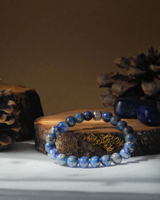 Bracelet en lapis lazuli naturel pose sur rondelle de bois avec pomme de pin et pierre polie de lapis lazuli