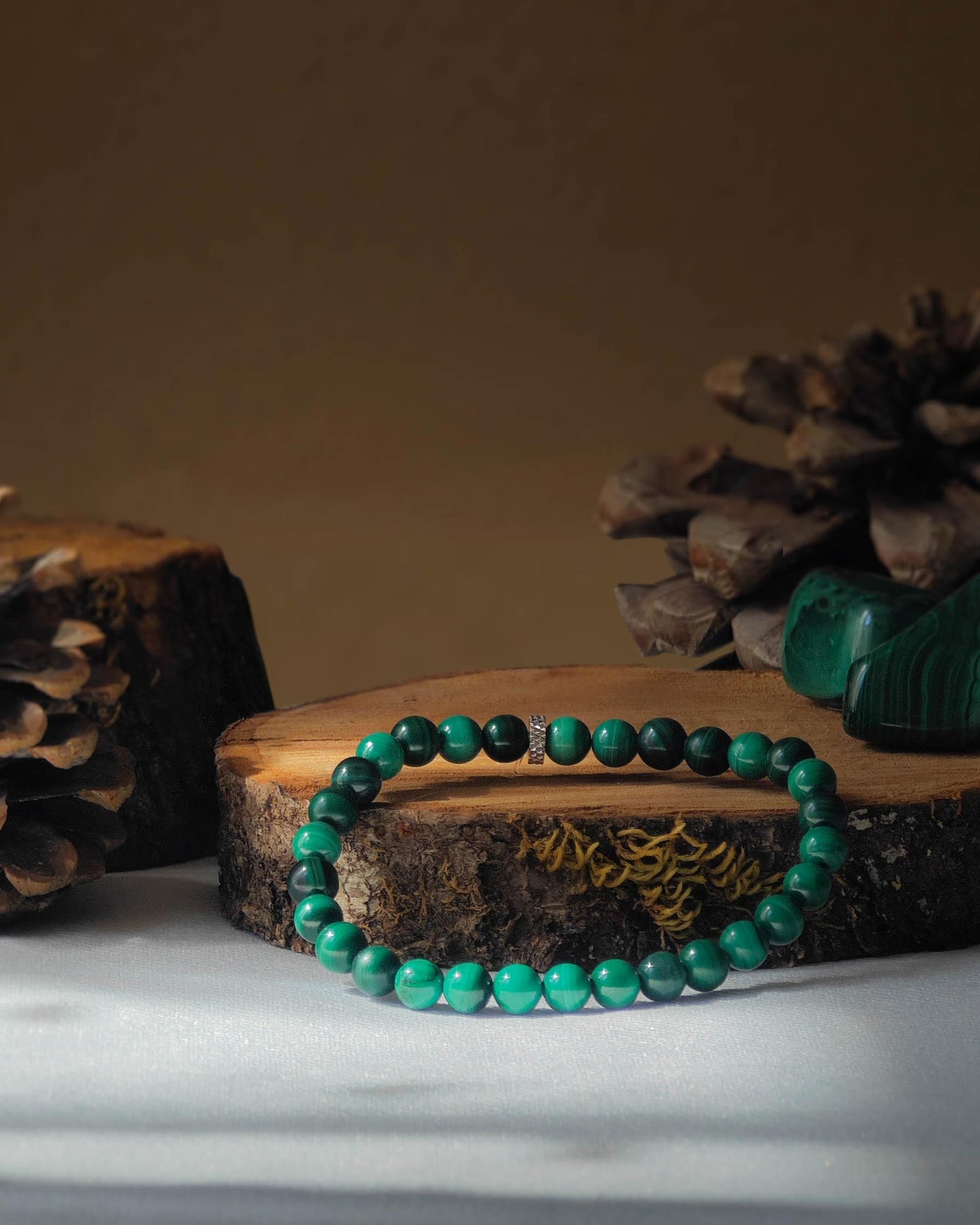 Bracelet en malachite naturelle pose sur rondelle de bois avec pomme de pin et pierre polie de malachite