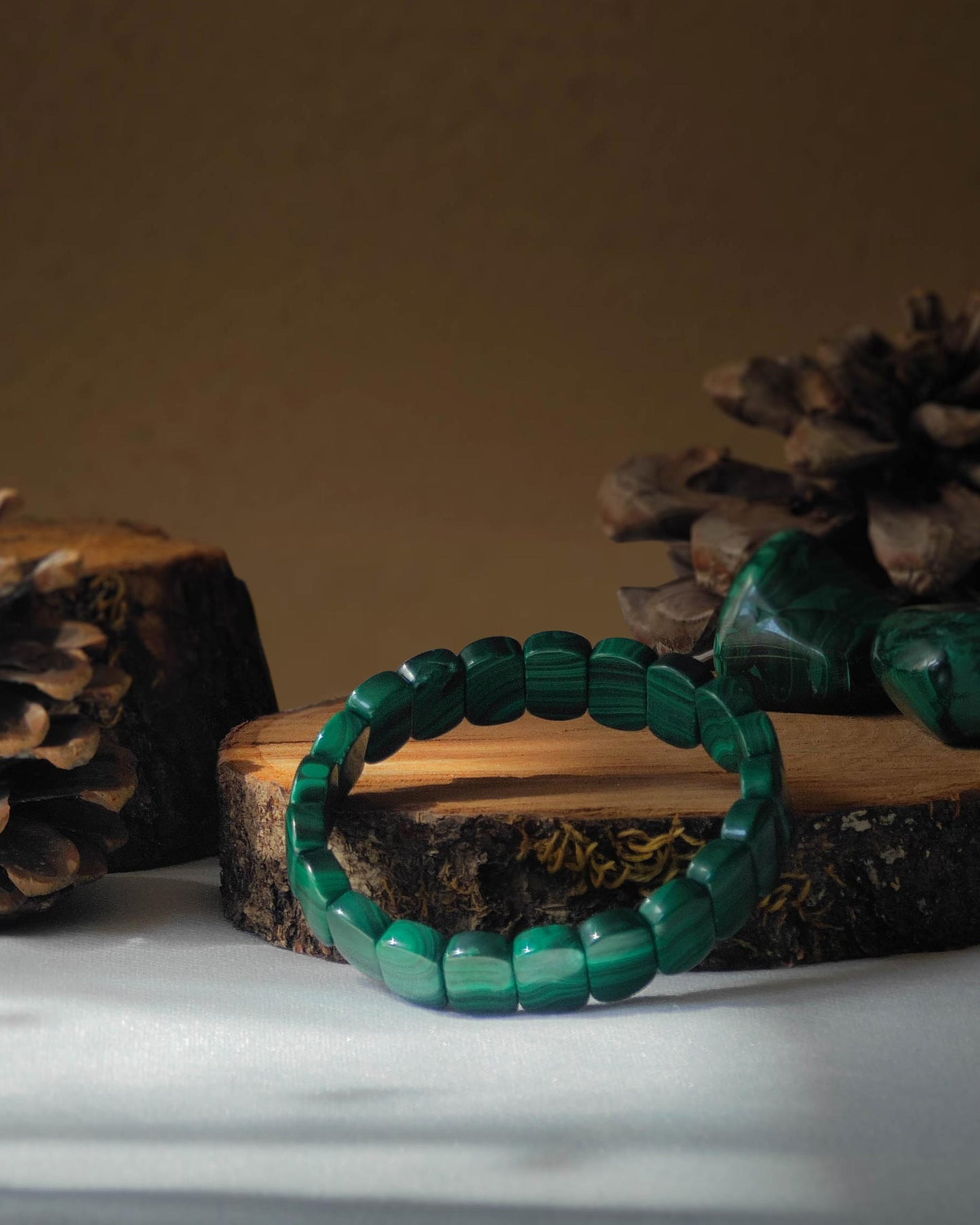 Bracelet en malachite perle plate pose sur rondelle de bois avec pomme de pin et pierre polie de malachite