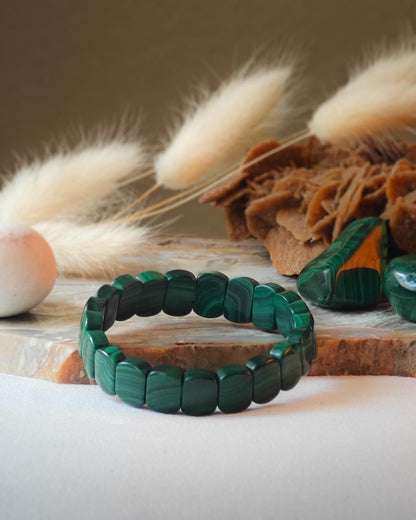 Bracelet en malachite perle plate pose sur roche lisse avec epis blancs et pierre polie de malachite