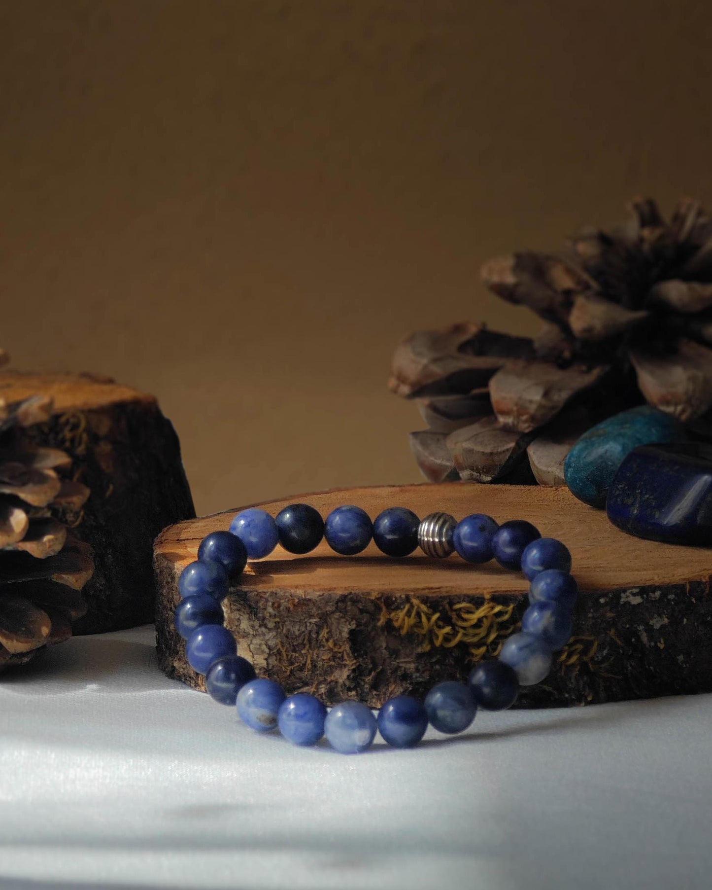 Bracelet en sodalite naturelle pose sur rondelle de bois avec pomme de pin et pierre polie de sodalite