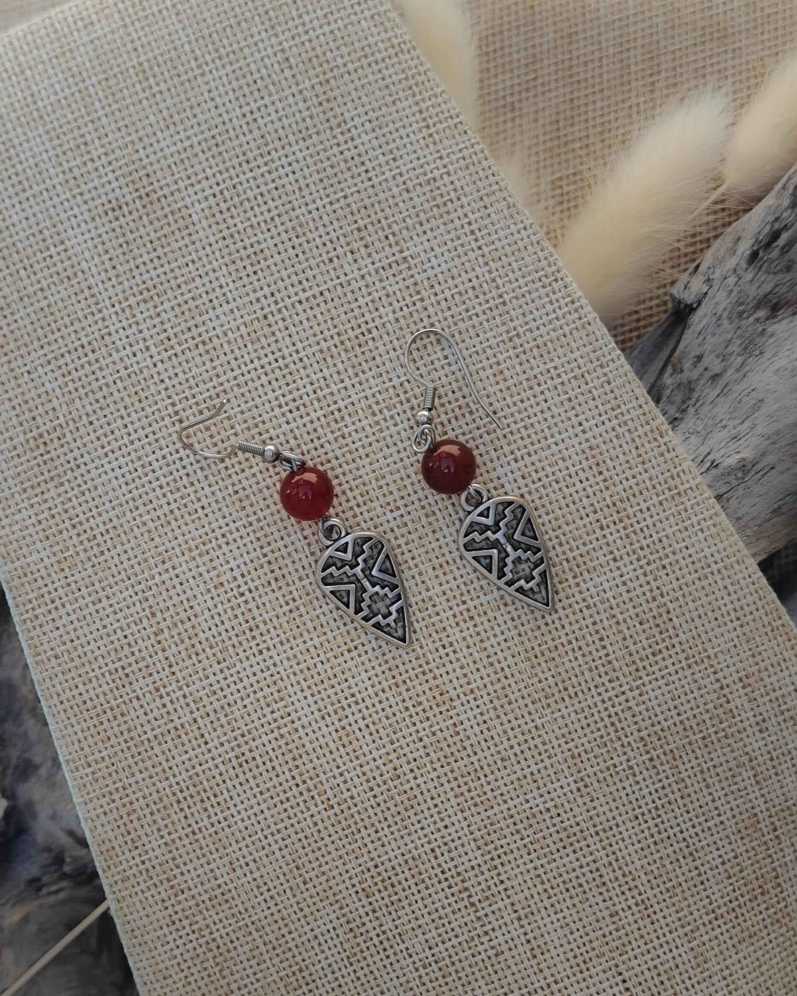 Vue de dessus des boucles d’oreilles Cornaline Bouclier acier montrant les détails de la pierre et du motif protecteur